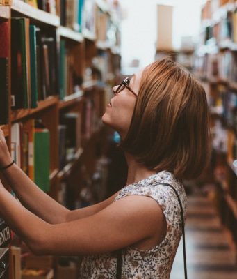 Una mujer busca entre las estanterías de una biblioteca.