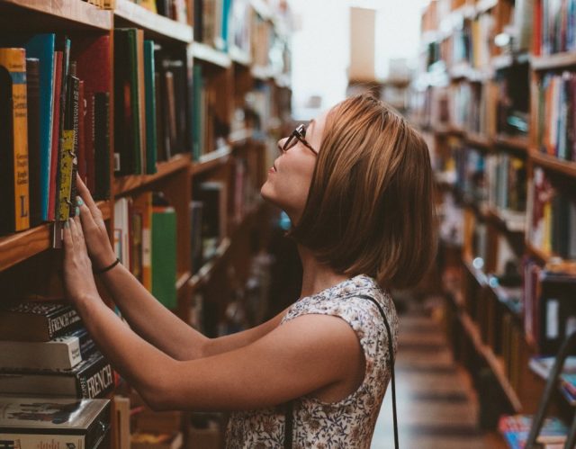 Una mujer busca entre las estanterías de una biblioteca.